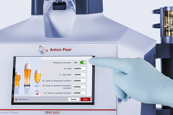 Gloved hand adjusting temperature correction settings on the touchscreen of the Anton Paar TPO 5001 Total Package Oxygen Meter.
