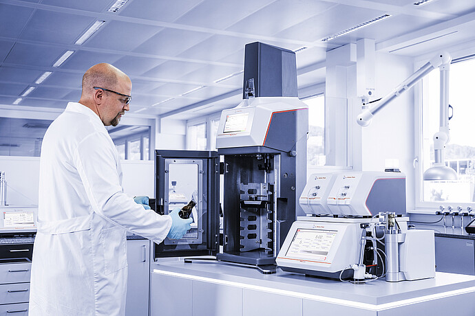 Lab technician loading a beer bottle into the Anton Paar TPO 5001; DMA 4501 M and PFD filling device visible in the background.